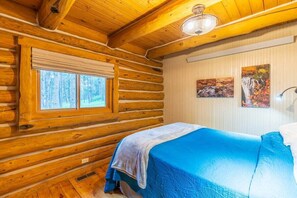 A log cabin room with a bed, a window, and two paintings on the wall. - Pine Cabin- Log cabin close to Custer (Custer)