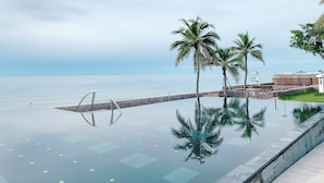 Una piscina infinita tranquila con vistas despejadas al mar, palmeras y una pared de piedra.