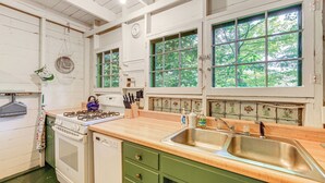 Une cuisine équipée d’une cuisinière, d’un four et d’un évier, avec des meubles en bois et une fenêtre donnant sur des arbres.