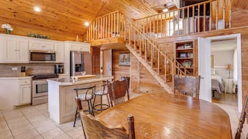 Une cuisine spacieuse dotée d’un îlot central, d’un escalier en bois et d’un coin repas avec une grande table et des chaises.