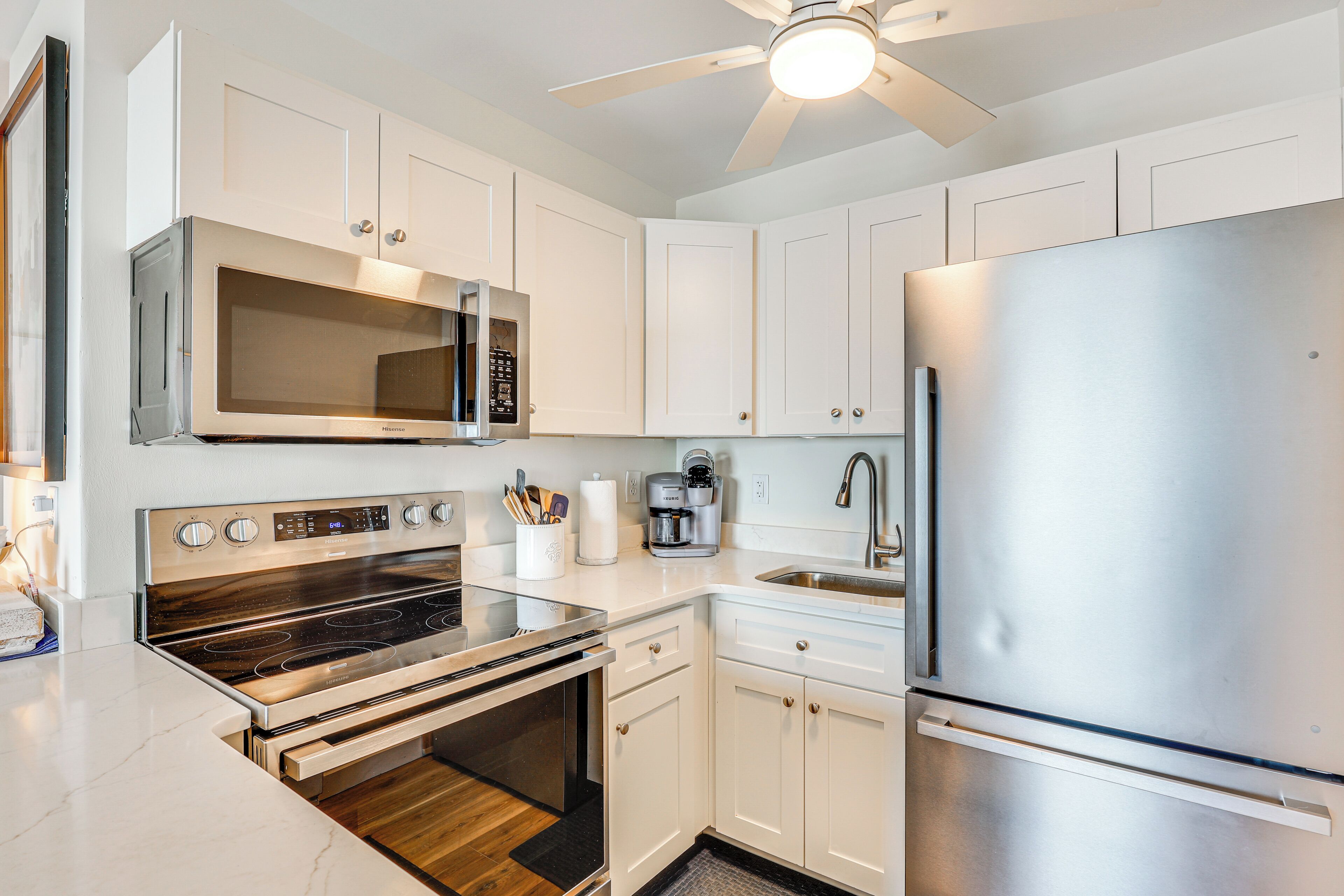 A modern kitchen with stainless steel appliances, white cabinetry, and a ceiling fan.
