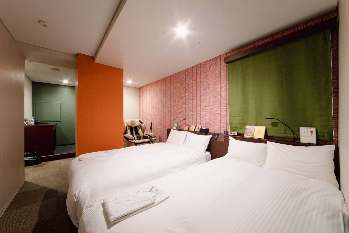 A hotel room with two beds, a massage chair, a desk, and a green curtain.