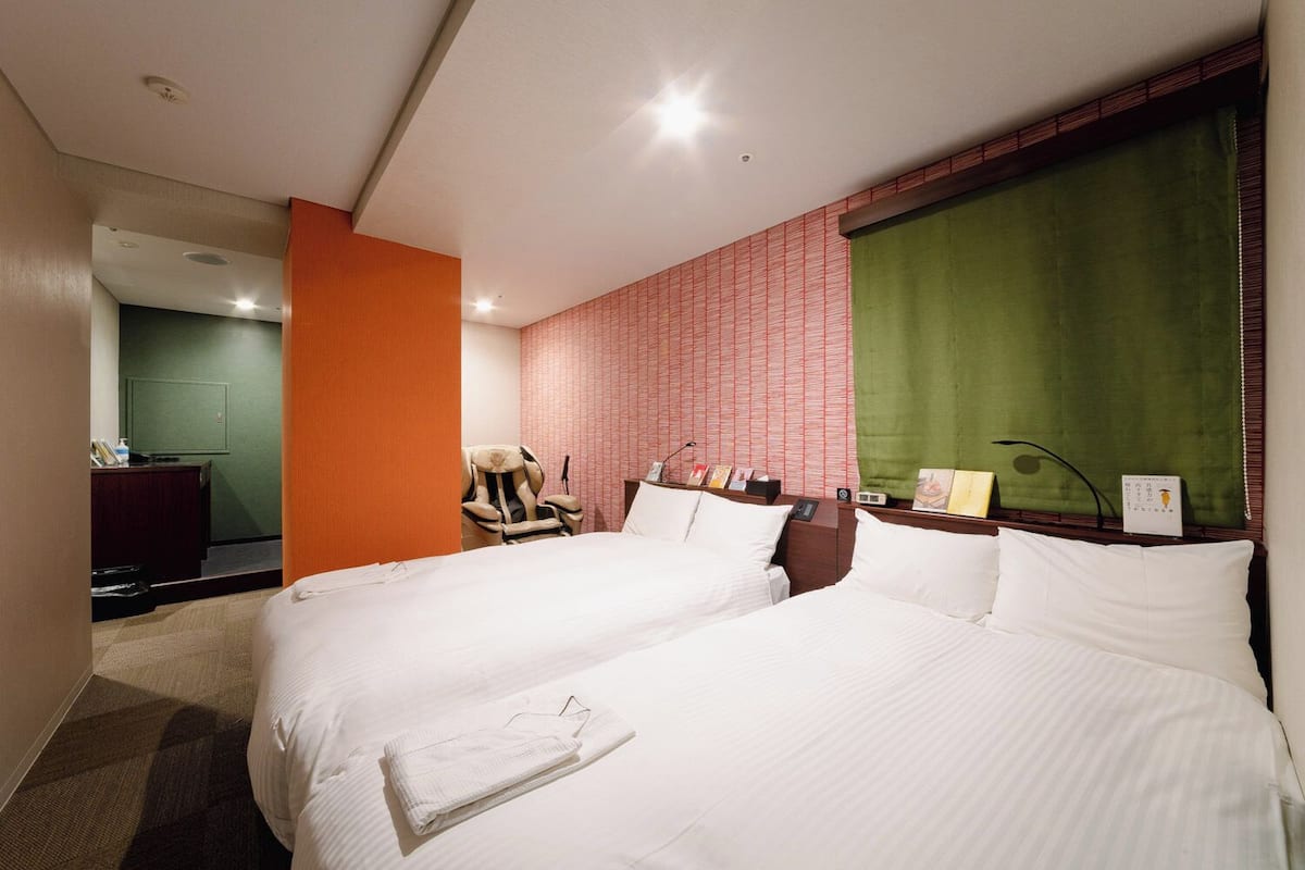 A hotel room with two beds, a massage chair, a desk, and a green curtain.