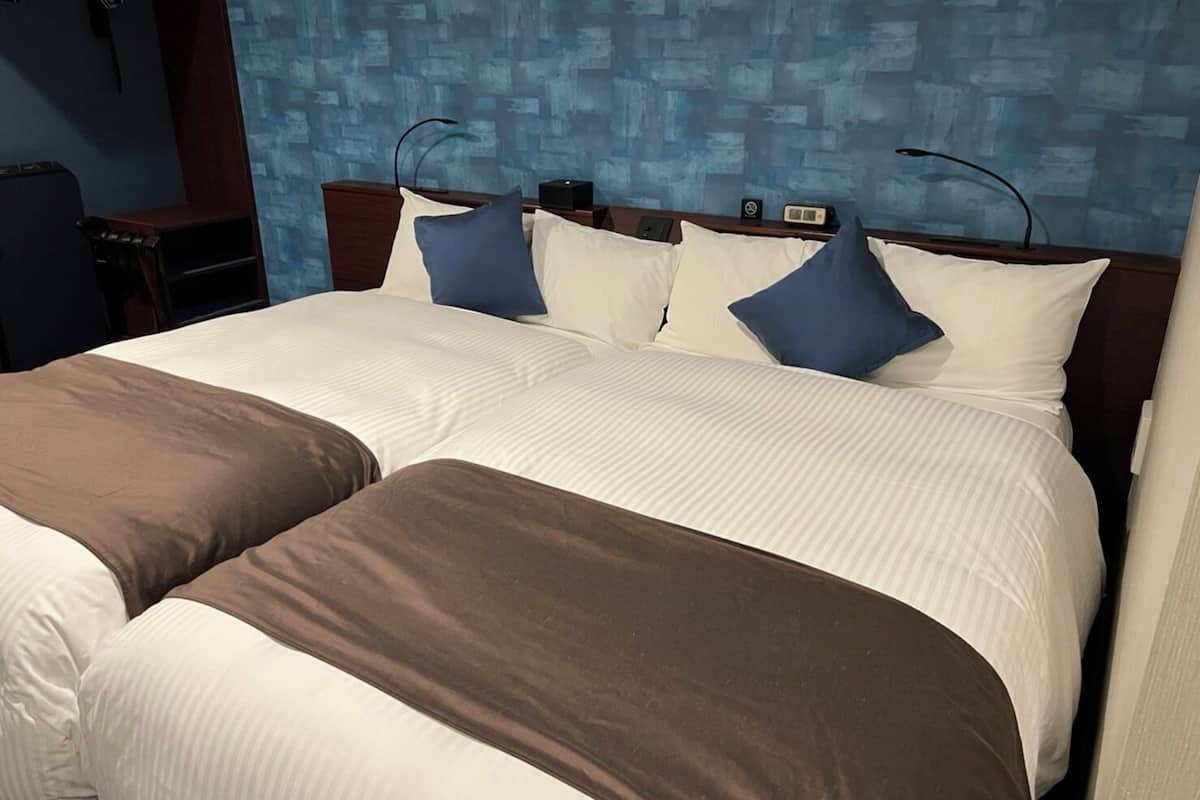 A hotel room with two beds, a nightstand, a lamp, and a clock on the wall.