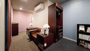 Una habitación de hotel con escritorio, dos sillas, una estantería, un armario y un equipo de aire acondicionado.