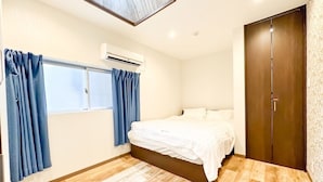 A bedroom with a bed, a window with curtains, an air conditioning unit, and a wooden floor.