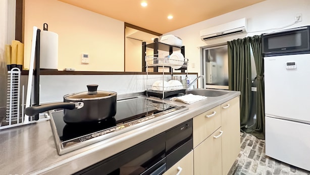 A modern kitchen with a stove, sink, and dishwasher. There is a dish rack above the stove and a refrigerator to the right.