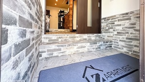 A modern apartment entrance with stone walls, a wooden door, and a blue mat with 'APARTMENT' on it.