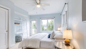 Quarto com cama, duas luminárias de cabeceira, ventilador de teto, janela e porta.