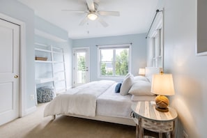 A bedroom with a bed, two bedside lamps, a ceiling fan, a window, and a door.