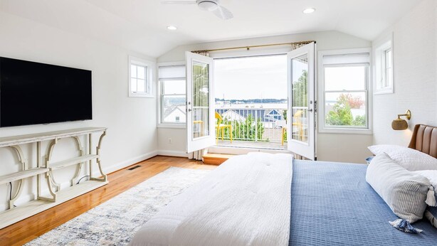 Quarto com cama grande, TV e varanda com vista para edifícios e vegetação.