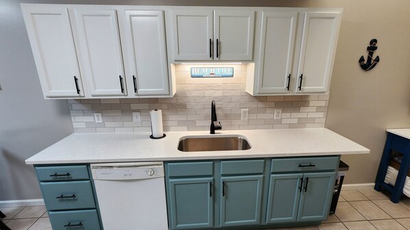 A kitchen with white upper cabinets, a stainless steel sink, and teal lower cabinets.