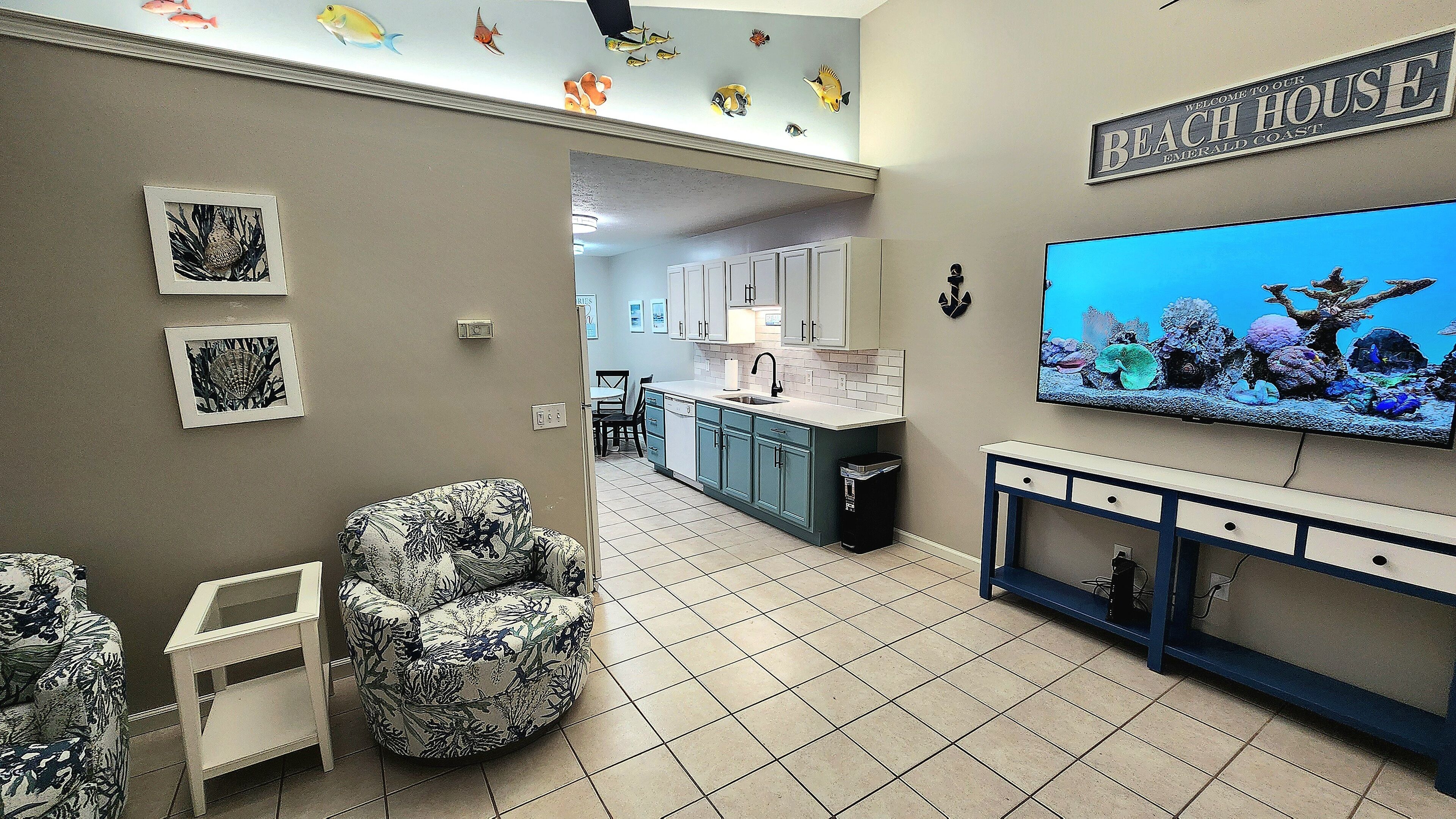 A modern kitchen with white cabinets, a large TV, and a fish-themed wall decal.