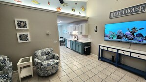 Une cuisine moderne avec des meubles blancs, un grand téléviseur et un décor mural sur le thème des poissons.