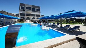 A swimming pool with blue umbrellas, lounge chairs, and a building in the background. - Ketrin Hotel & Restaurant (Masis)