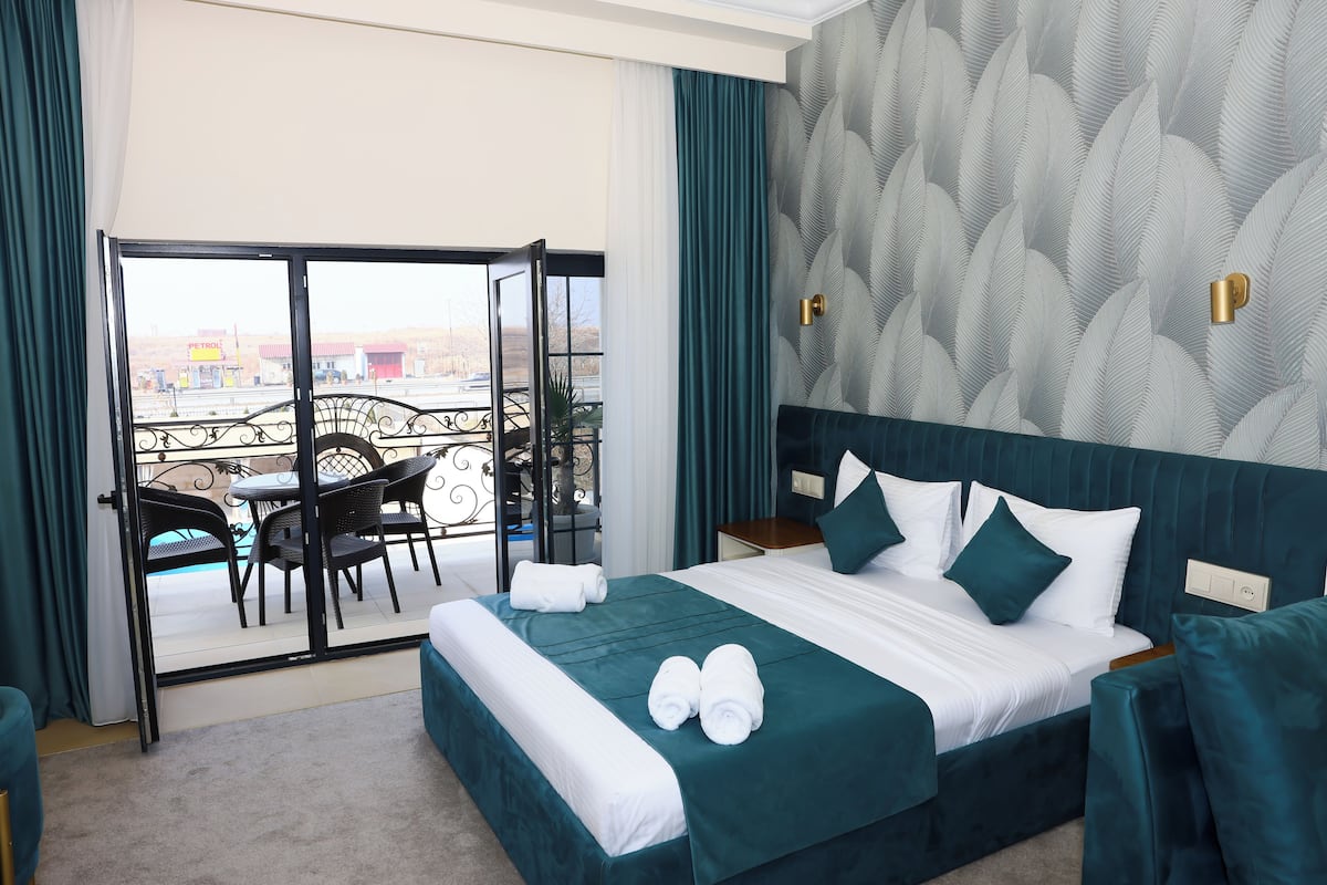 Une chambre d’hôtel dotée d’un grand lit, d’un balcon avec mobilier d’extérieur et offrant une vue sur le paysage urbain.