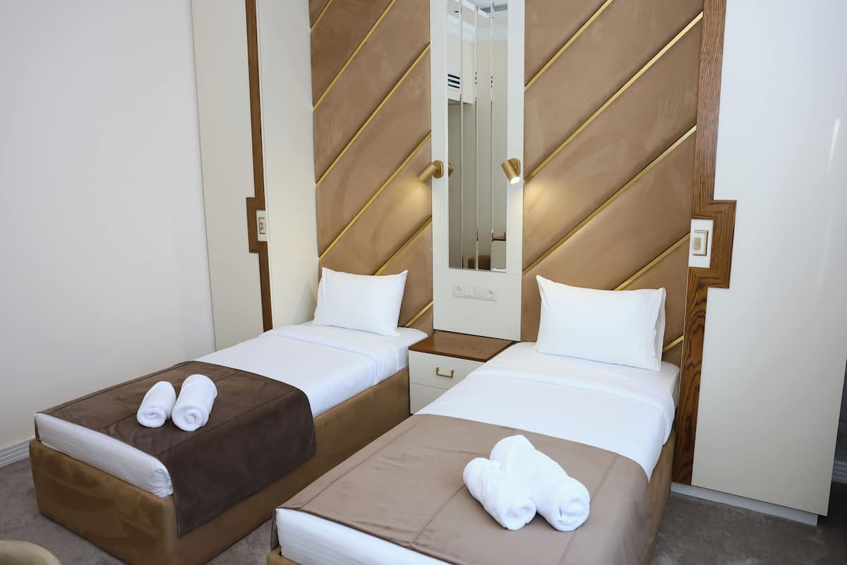 Une chambre d’hôtel avec deux lits, chacun doté d’une tête de lit marron et de draps blancs. Il y a des serviettes sur les lits et un miroir sur la tête de lit.