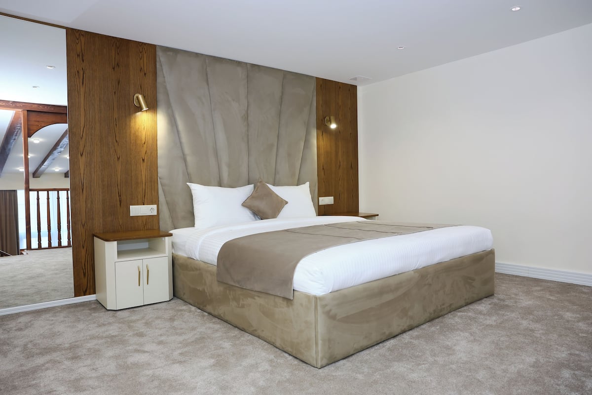 Une chambre à coucher avec un grand lit, une tête de lit en bois, des tables de chevet et un miroir.
