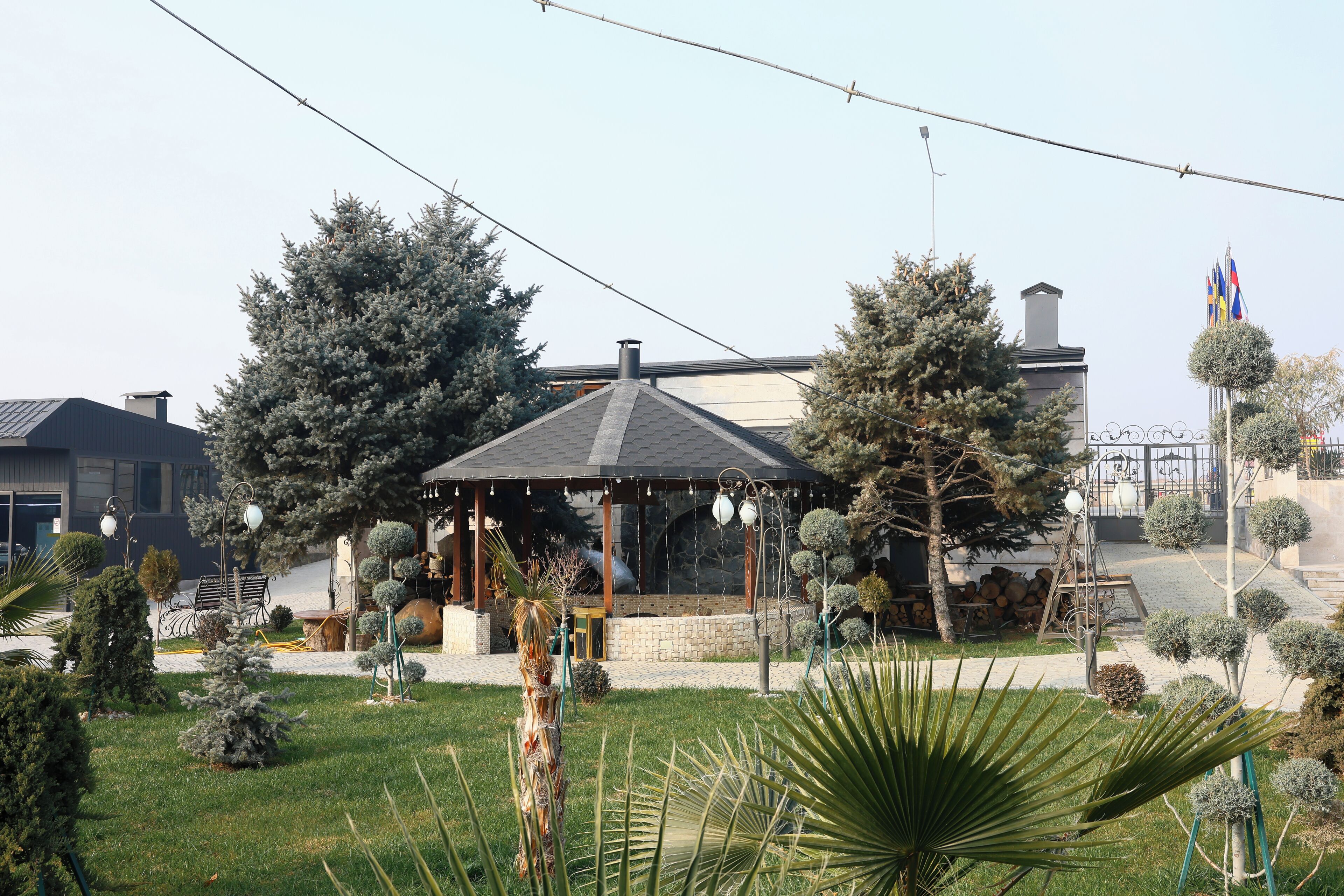 A gazebo with a tiled roof surrounded by neatly trimmed trees and a lawn.