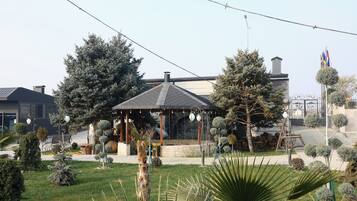 A gazebo with a tiled roof surrounded by neatly trimmed trees and a lawn.