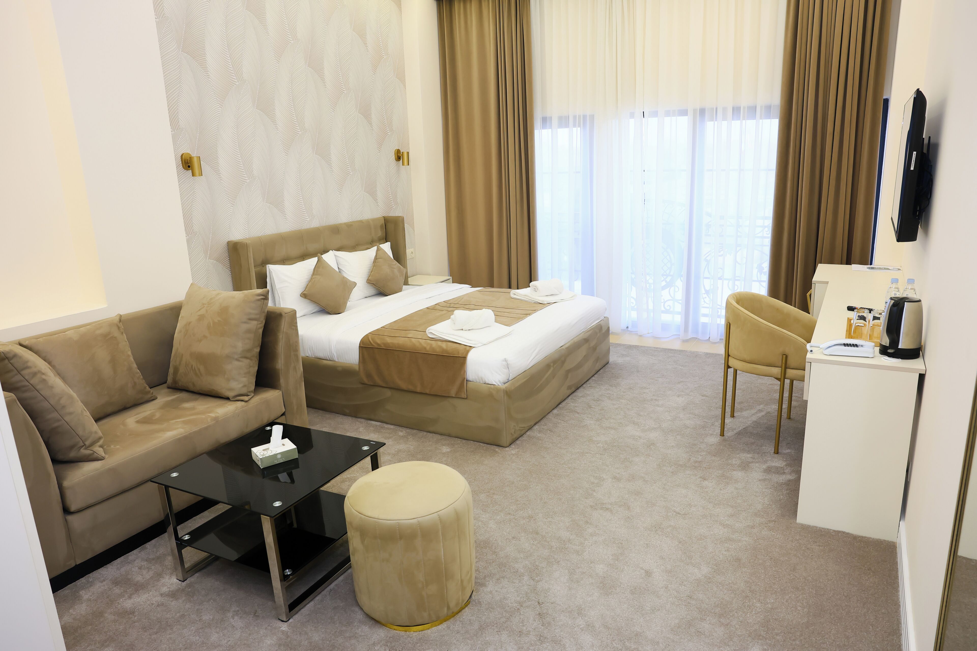 A hotel room with a bed, a sofa, a desk, and a small ottoman.