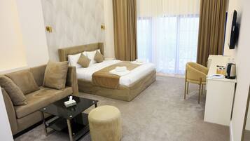 A hotel room with a bed, a sofa, a desk, and a small ottoman.