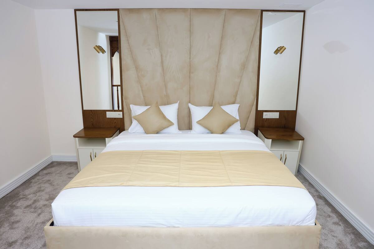 Une chambre à coucher avec un grand lit, deux tables de chevet, une tête de lit et un miroir.