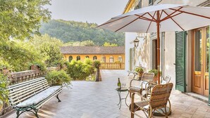 An outdoor patio with a bench, wicker chairs, and a table with a bottle and glasses. - Villa Margaret: A splendid nineteenth-century three-story historical villa surrounded by the greenery, with Free WI-FI. (Pontremoli)