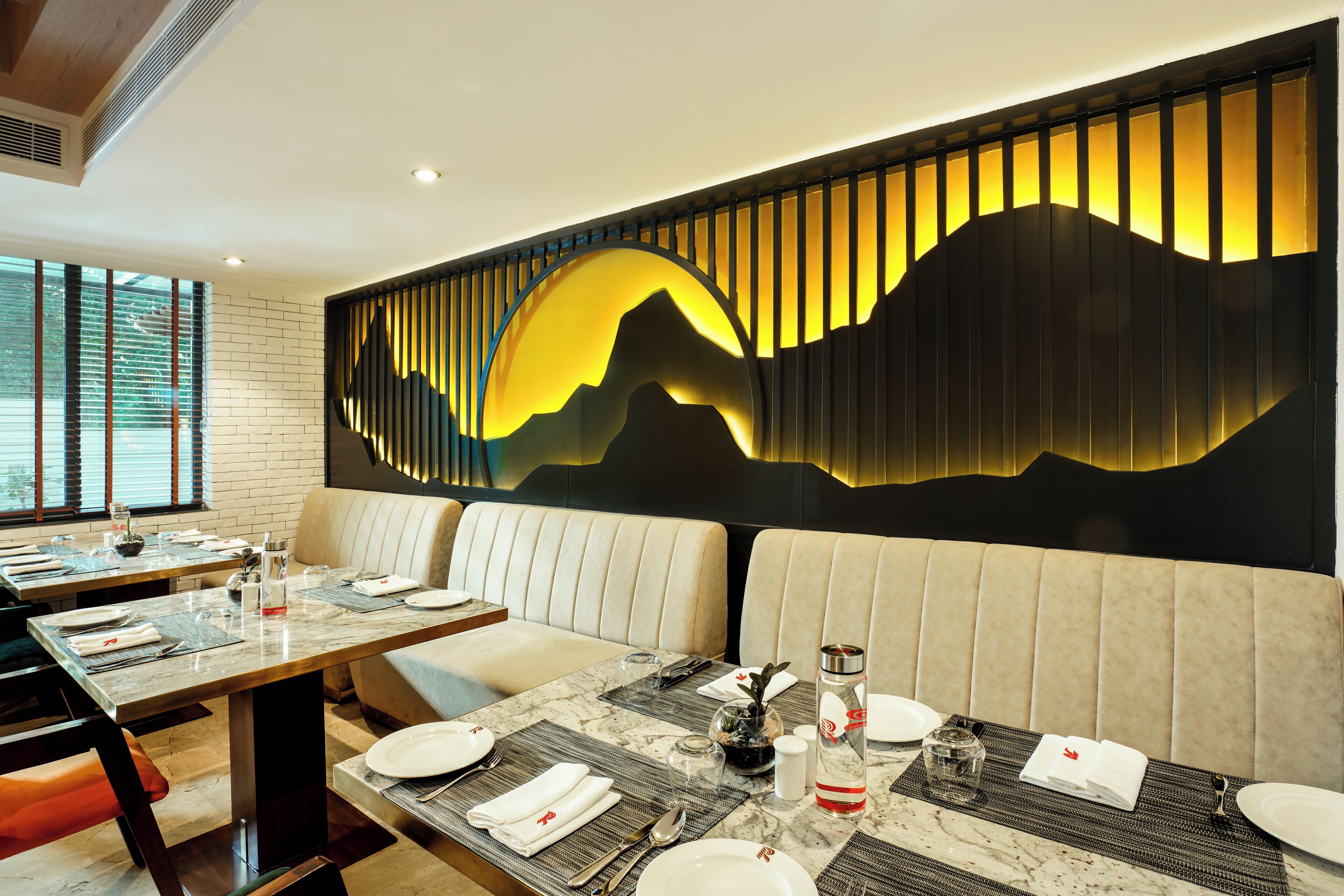 A restaurant with a modern interior, featuring a large wall mural, plush seating, and a well-set dining table.