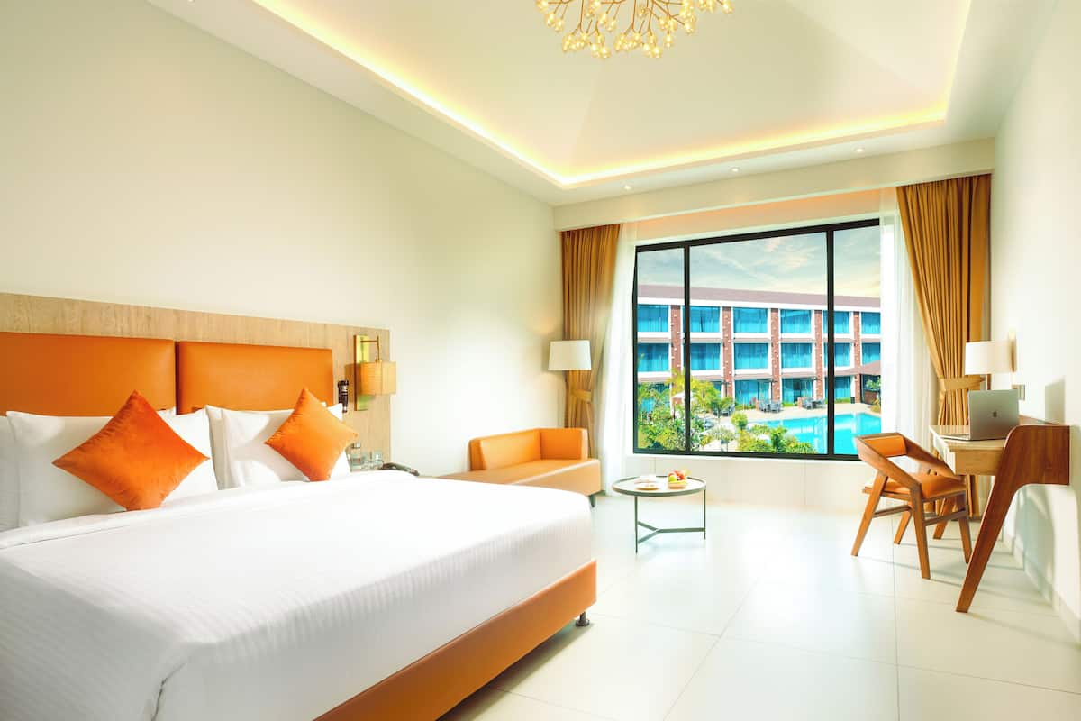 A hotel room with a large bed, a desk, a chair, and a view of a swimming pool.