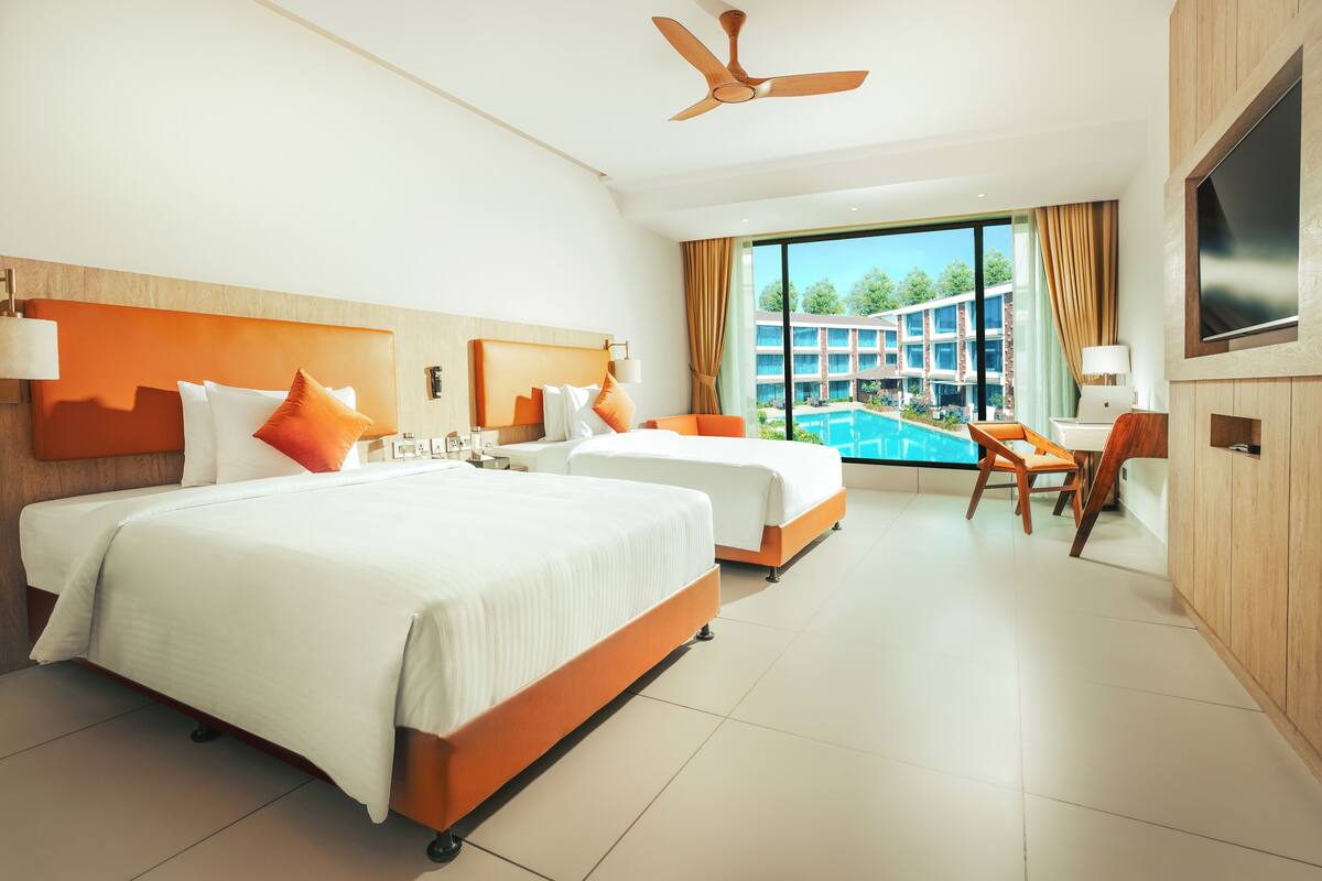A hotel room with two beds, a ceiling fan, a TV, and a view of a swimming pool.