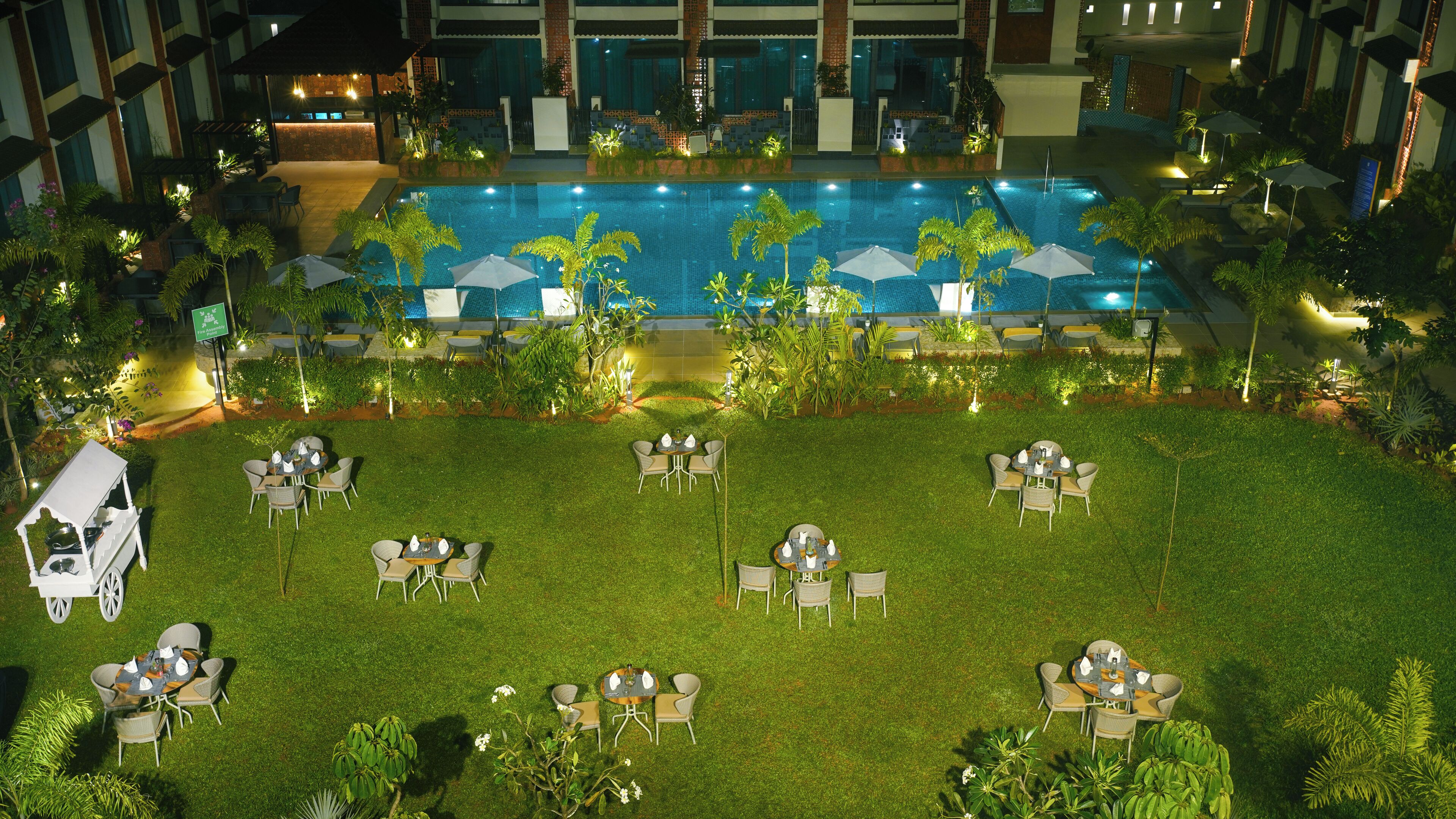 Un espace piscine extérieur doté de plusieurs coins salon et de parasols, entouré d’une végétation luxuriante et d’une pelouse bien entretenue.