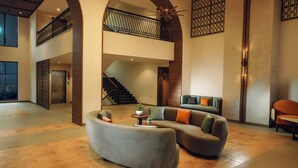 Un'ampia hall con un divano grigio curvo, una scala e un soppalco.