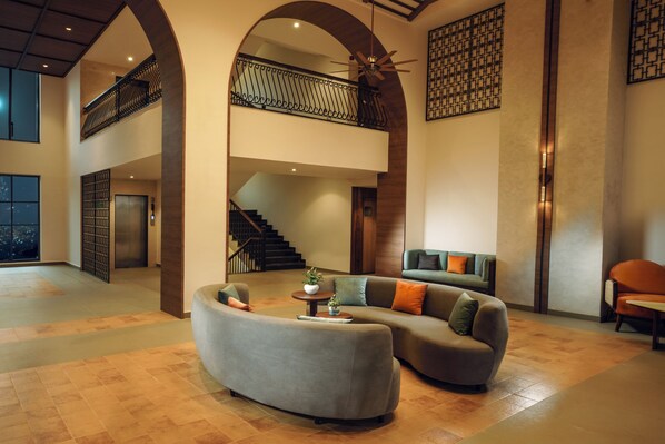 Eine geräumige Lobby mit einer gebogenen, grauen Couch, einer Treppe und einer Empore.