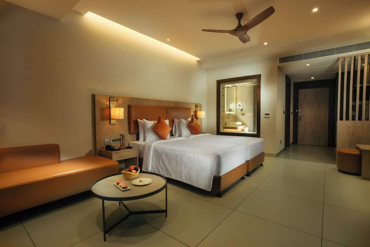 A modern hotel room with a large bed, a sofa, a small table, and a ceiling fan.
