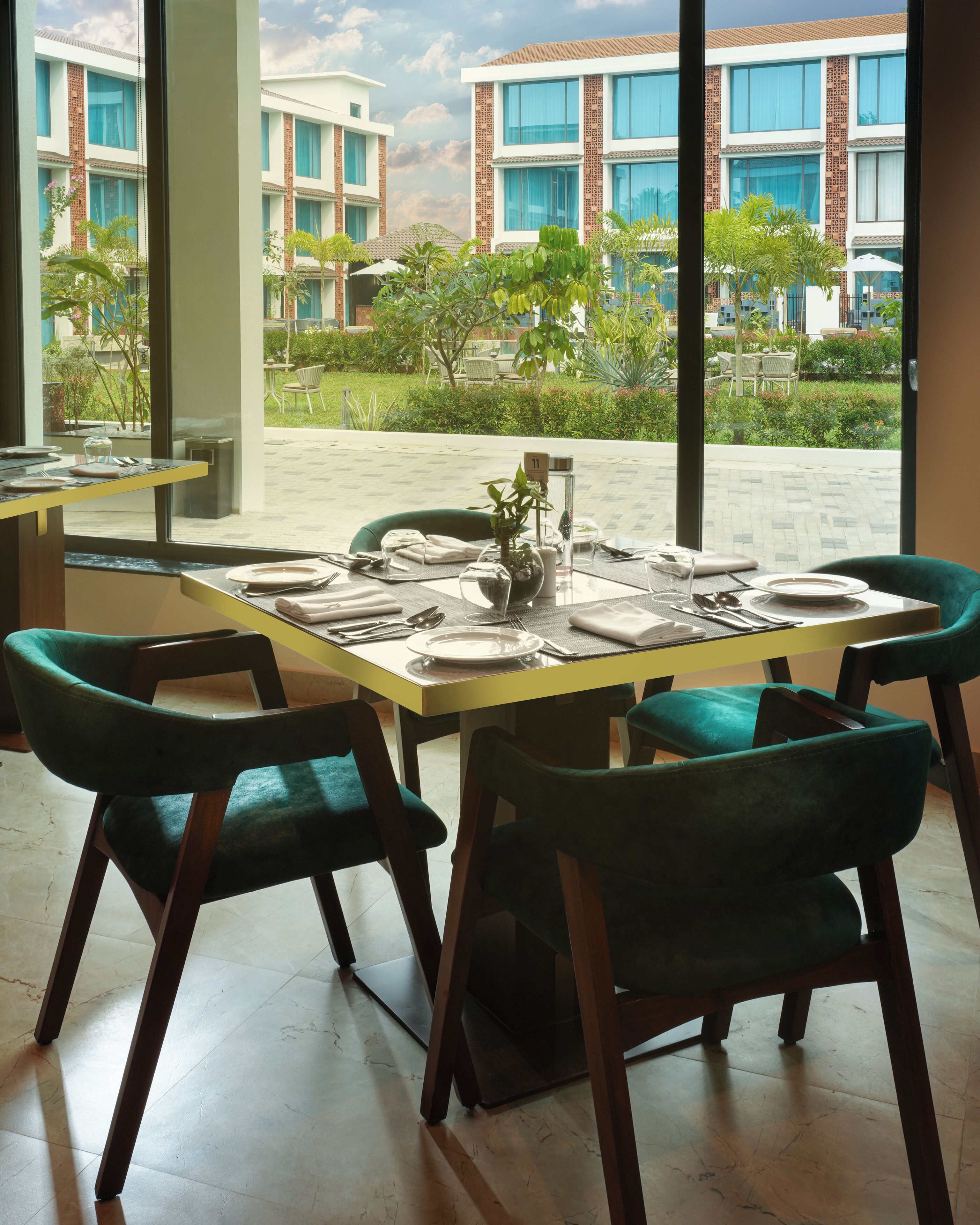 Comedor con mesa dispuesta para seis personas, ventanas amplias y vista a un edificio de varios pisos.