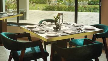 Comedor con mesa dispuesta para seis personas, ventanas amplias y vista a un edificio de varios pisos.
