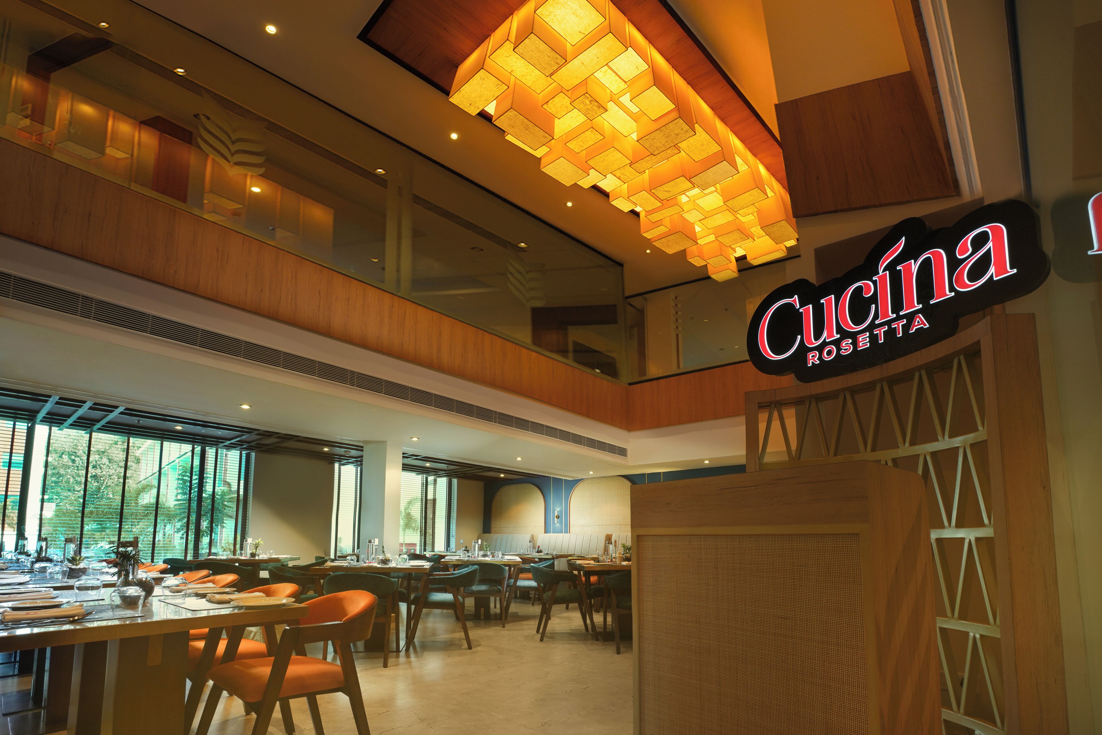 A restaurant interior with multiple dining tables and chairs, a prominent ceiling light fixture, and a sign reading "Cucina Rosetta".