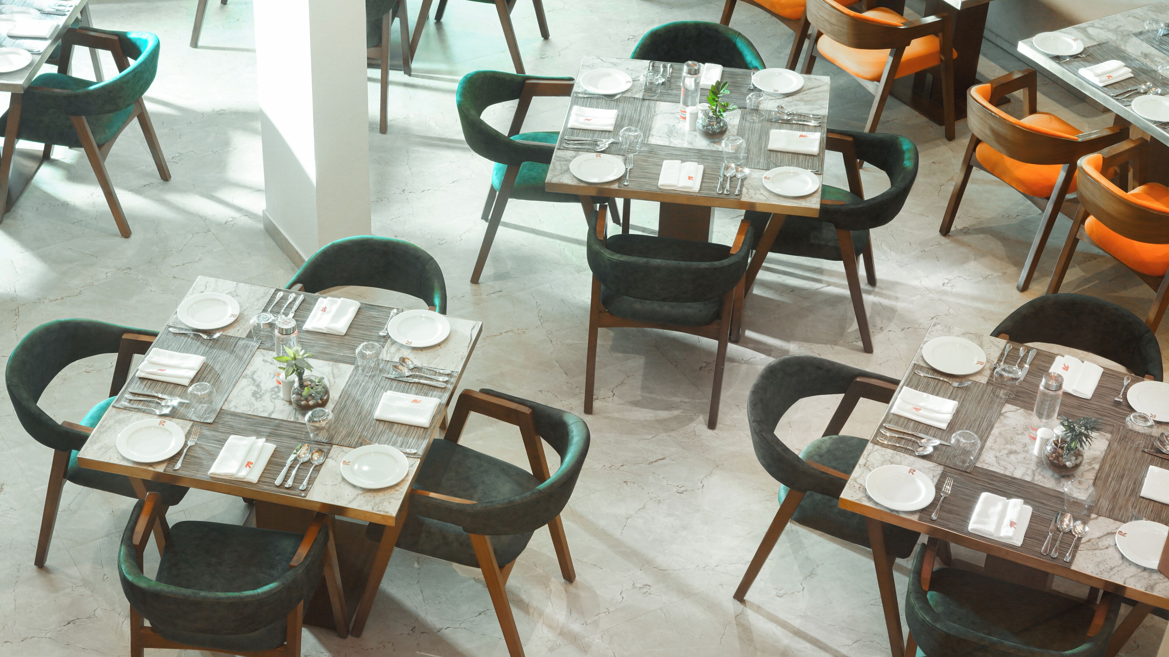 Un comedor con mesas dispuestas para cuatro, cada una con sillas verdes.