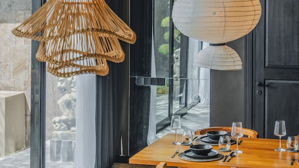 A modern dining area with a wooden table, chairs, and a unique woven light fixture. - Nebius Villa by Betterplace (Ungasan)