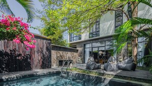 A modern outdoor pool area with a wooden fence, a stone wall, and a seating area with bean bags. - Nebius Villa by Betterplace (Ungasan)