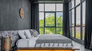 A modern bedroom with a large window, a bed with a wooden platform, and a wall-mounted decorative piece. - Nebius Villa by Betterplace (Ungasan)