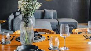 A dining area with a wooden table set for a meal, a vase with flowers, and a modern light fixture. - Nebius Villa by Betterplace (Ungasan)