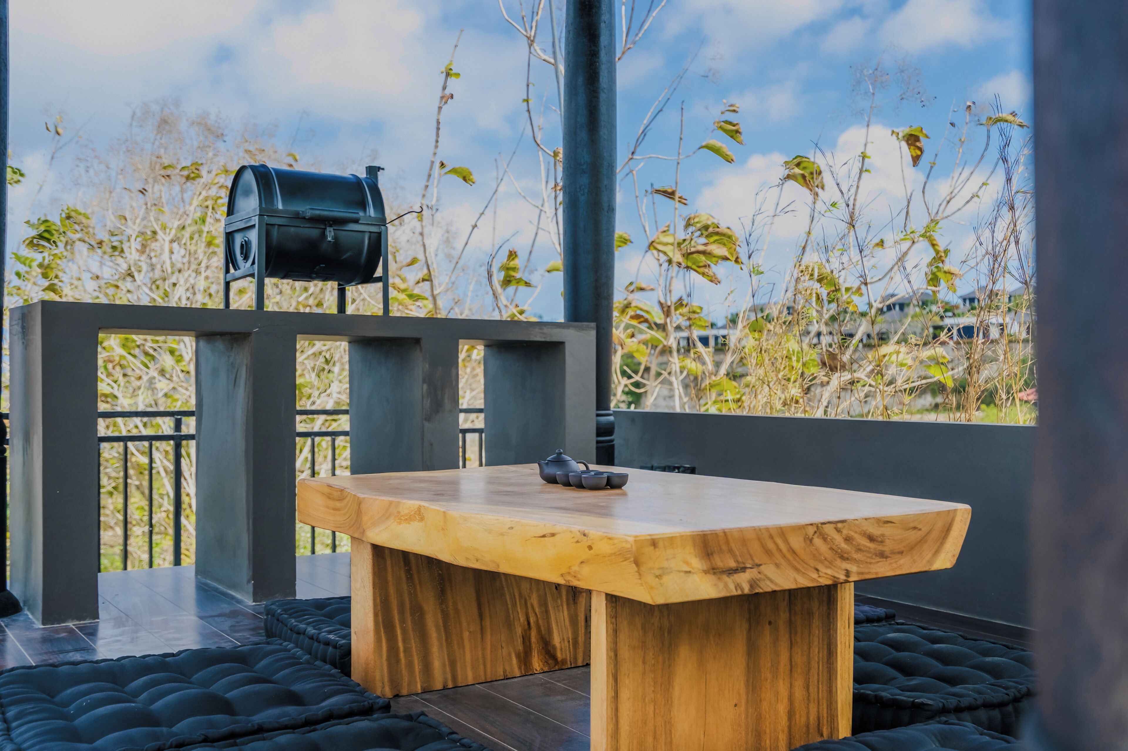 Una mesa de madera con una parrilla negra en un balcón con vista a árboles y edificios.