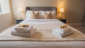 A hotel room with a large bed, two bedside lamps, and towels on the bed.