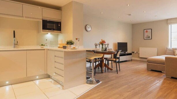 A modern kitchen with a microwave, a dining area with chairs, a sofa, and a clock on the wall.