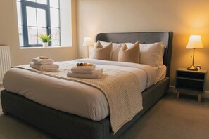 A neatly made bed with pillows, a bedside lamp, and a small nightstand with a lamp. - Gated Parking! Quiet block, lift,  Sleeps up to 4 (Cheshire West and Chester)