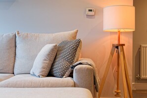A room with a sofa, pillows, a lamp, and a thermostat on the wall. - Chester Apartment. Gated parking + Lift Sleeps up to 4 (Cheshire West and Chester)