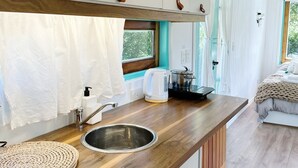 A modern kitchen with wooden countertops, a sink, and a window overlooking a bedroom with a bed and curtains.