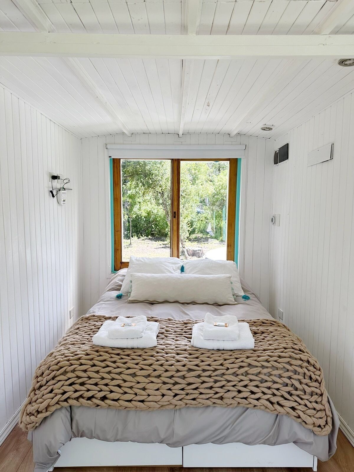 Une chambre à coucher avec un lit, une grande fenêtre et une vue sur la verdure.